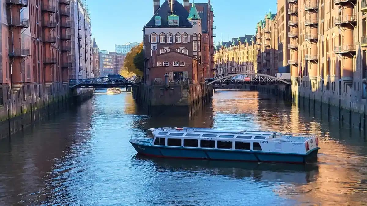 Hamburger Speicherstadt: Barkasse Allegra auf dem Wasser vor dem historischen Wasserschloss und typischen Backsteingebäuden